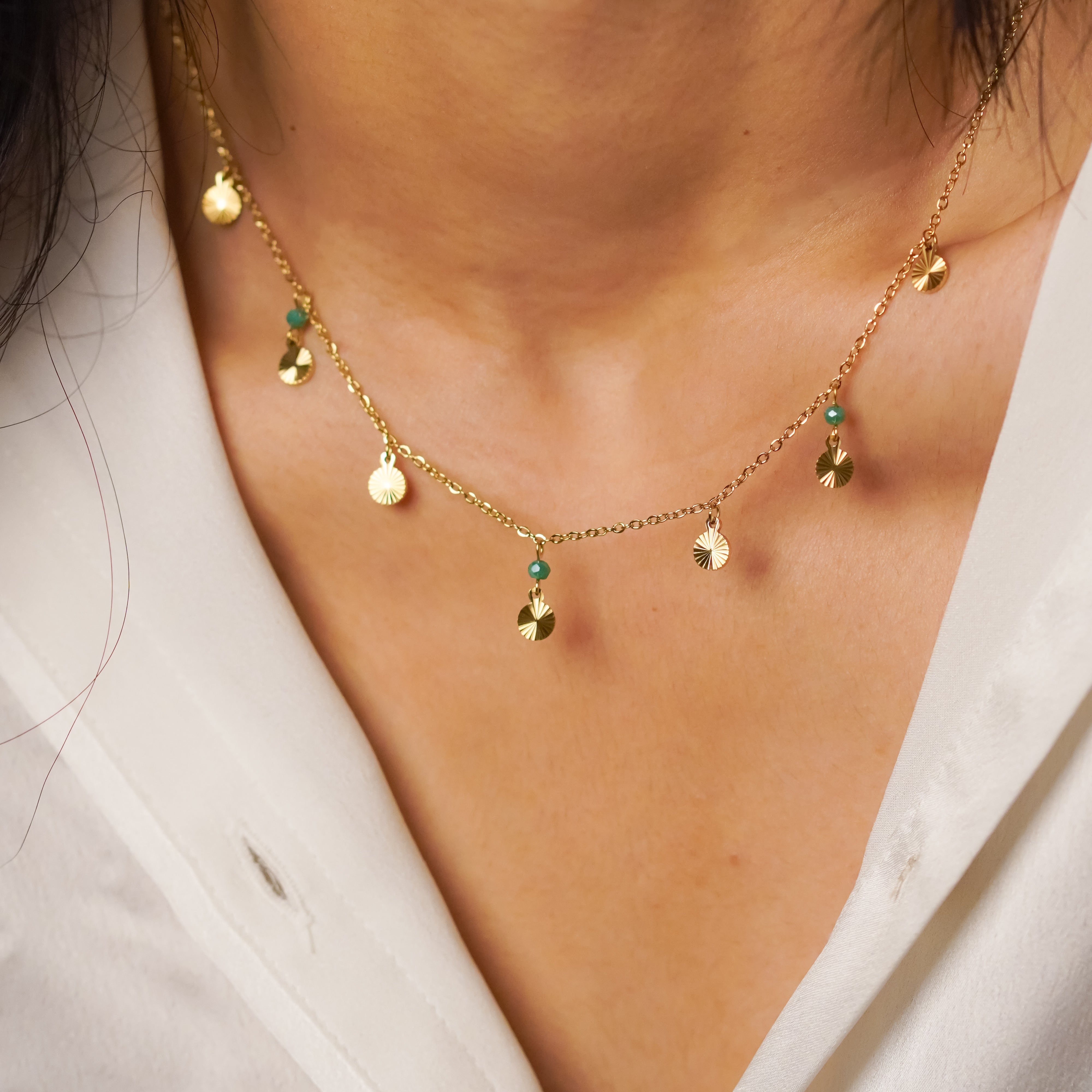 Gold necklace with small pendants on a person wearing a white shirt